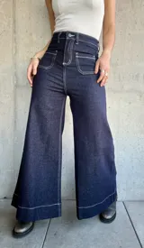 Pantalón de jean azul oscuro, de corte ancho, con bolsillos delanteros cuadrados y costuras blancas contrastantes.