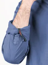 Camisa azul de hombre confeccionada en 100% algodón twill, tintada en prenda. Cuenta con corte regular fit, cuello button-down, cierre frontal de botones, manga larga con puño simple y pequeño logo rojo bordado en el pecho.