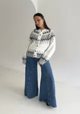 Cardigan de punto con diseño jacquard de inspiración nórdica, en tonos blanco, gris y marrón. Presenta cuello redondo, cierre frontal con botones y mangas largas con puños acanalados.