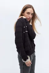 Sweater de punto negro con detalle de calados y lazo en el escote. Tiene ribetes con volados en contraste en el cuello y puños.