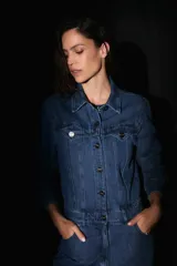 Mono de denim azul con cierre frontal de botones metálicos, cuello camisero, mangas largas y bolsillos delanteros.