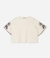 Blusa de corte boxy en color crudo, con cuello redondo y mangas cortas estilo godê. Presenta detalles de bordado floral en tonos marrones en ambas mangas.