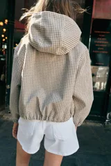 Cazadora con capucha ajustable, manga larga con puños elásticos, bolsillos delanteros y bajo ajustable con cordones. Cierre frontal con cremallera y diseño estampado a cuadros.