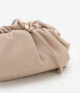 Cartera transversal pequeña color beige, confeccionada en poliuretano con diseño fruncido y asa fina de cordón con detalles metálicos.