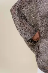 Buzo de tejido liviano y calado con brillo sutil, color gris oscuro o negro. Presenta un calce amplio y mangas amplias, con un detalle de tiras entrelazadas en la espalda. El largo es irregular, más largo en la parte trasera.