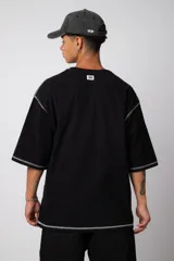 Remera de corte oversize color malva, confeccionada en algodón pesado, con costuras externas visibles en color blanco que recorren el centro, el cuello y los bordes de las mangas.