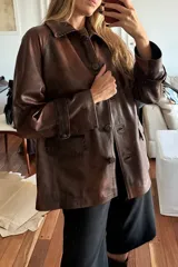 Tapado de cuero marrón con diseño artesanal, cuello camisero con detalles de pasamanería en gamuza, cierre frontal con botones de guampa y bolsillos delanteros con bordes decorativos. Presenta un corte cómodo y versátil.