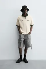 Bermuda de corte relajado en denim de algodón color beige, estilo cargo, con cinco bolsillos y bolsillos plastrón con solapa en las perneras.