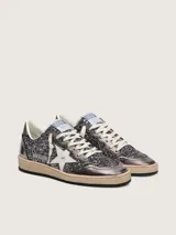 Zapatillas Golden Goose modelo Ball Star de estilo retro, con empeine y lengüeta cubiertos de glitter gris oscuro y detalles en cuero laminado. Presentan la clásica estrella lateral en cuero blanco, puntera reforzada y cordones de algodón crudo, con suela de goma desgastada.