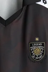 Camiseta de futbol de manga corta con corte holgado, color negro con estampa sutil y bandas blancas con rombos en las mangas. Presenta cuello en V con solapa y esc11udo bordado en el pecho.