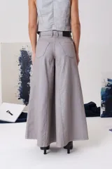 Pantalón tipo palazo de tiro medio, confeccionado en denim de algodón con acabado metalizado. Presenta cierre frontal con botón metálico, bolsillos delanteros y traseros, y una silueta amplia de pierna ancha.