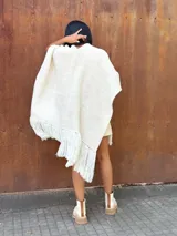 Ruana tejida de lana en color crudo, con diseño de flecos en los bordes. Es una prenda versátil y abrigada, ideal para complementar diversos looks.