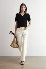 Sweater de punto negro de manga corta con cuello polo y ribetes contrastantes en color beige con detalles de encaje en el cuello y los puños.