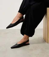 Zapatilla tipo slingback de cuero negro con textura de piel de serpiente, diseño destalonado con tira elástica trasera y punta fina.