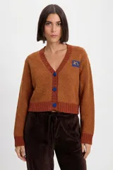Cardigan corto de tejido de punto texturado en tonos terracota y amarillo, con escote en V, botones azules a contratono y parche bordado en el pecho.