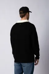 Sweater de punto con textura waffle en color blanco, con cuello polo en contraste color verde oscuro y cierre frontal de botones. Presenta un bordado decorativo en el pecho y un corte relajado.