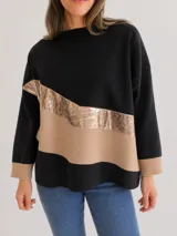 Buzo de tejido suave con diseño oversize y calce relajado. Presenta un diseño de bloques de color en negro y beige, con una franja diagonal en material metalizado dorado. Cuenta con cuello redondo, mangas largas y puños tejidos en color beige.