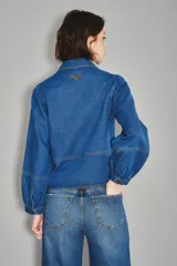 Camisa crop de denim azul, con cuello camisero, botones frontales dorados, dos bolsillos en el pecho y mangas abullonadas.