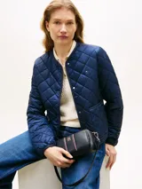 Cartera bandolera Tommy Hilfiger de color azul marino, con acabado granulado, cierre de cremallera superior, compartimento principal y bolsillo exterior con cremallera. Incluye correa extraíble para el hombro, detalles distintivos con franjas verticales y la insignia del monograma TH en metal dorado en la parte delantera.