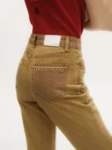 Pantalón de denim color tostado con tiro alto y corte oxford. Presenta detalles de apliques metalizados a lo largo de las costuras laterales y en los bolsillos.