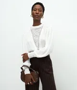 Blusa de viscosa color blanco con cuello alto, mangas largas con puños ajustados y detalles de encaje bordado en el frente y en los puños.