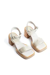 Sandalias de taco cuadrado medio, con base y talón en gamuza color tostado. Presenta una tira frontal de múltiples bandas doradas y una pulsera al tobillo con hebilla metálica.