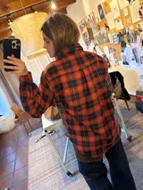 Camisa de corte amplio confeccionada en tela suave con diseño de paneles en diferentes estampados de cuadros escoceses en tonos verde, rojo y marrón. Presenta detalles bordados en el frente que incluyen un sol, un caballo y una bandera. Cuenta con cuello clásico y cierre frontal con botones.