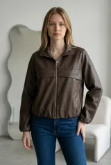 Campera tipo bomber de ecocuero color marrón chocolate, con cierre frontal completo, cuello alto y puños elásticos. Presenta un diseño con costura horizontal en el pecho y bolsillos laterales con cierre.