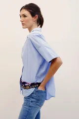 Camisa de manga corta celeste con rayas finas blancas, cuello camisero, cierre frontal con botones y corte amplio.