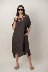 Vestido midi de lino color beige, de corte holgado y silueta acampanada. Cuenta con cuello redondo, mangas cortas amplias, bolsillos laterales y detalles de recortes horizontales en la falda con terminación asimétrica más larga en la parte trasera.