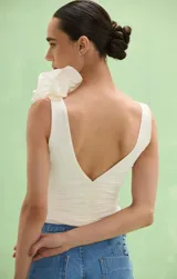 Top off white con escote en V y diseño drapeado en el torso. Cuenta con tiras anchas, destacándose una de ellas por estar decorada con apliques de flores volumétricas de tela.