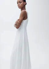Vestido midi de algodón blanco con diseño evasé, cuello cuadrado y tirantes anchos. Presenta un tejido bordado con detalles calados y costuras horizontales que crean un efecto de paneles.