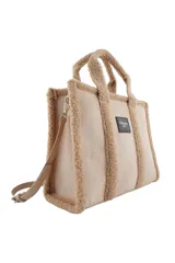Cartera tipo tote de Las Oreiro, confeccionada en gamuza sintética color beige con detalles de corderito en los bordes y manijas. Incluye un parche frontal con el logo de la marca y correa ajustable extraíble.