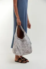 Bolso tipo tote de gran tamaño con acabado efecto craquelado en tonos blanco y gris. Presenta una estructura holgada, base amplia y correas integradas al diseño para llevar al hombro.