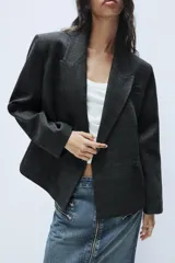 Blazer corto de corte oversize con estampado de cuadros, cuello con solapa de muesca, manga larga y cierre frontal cruzado con un botón. Cuenta con bolsillos decorativos de vivo en el frente y forro interior.