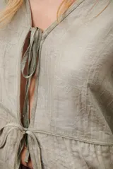 Chaqueta ligera de manga larga en color azul, con escote en V y cierre frontal mediante dos lazos ajustables. Presenta un diseño fluido con textura sutil y corte recto.