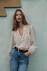 Blusa de escote en pico con volantes frontales, manga larga con puños elásticos y cierre frontal con botones.