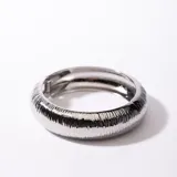 Brazalete rígido plateado con textura acanalada y cierre de bisagra.