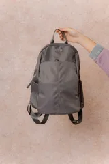 Mochila compacta de color beige, con compartimento principal con cierre, bolsillos laterales y bolsillo frontal con cierre oculto. Cuenta con correas regulables y acolchonadas y asa superior.