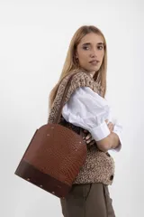 Matera tipo cartera de cuero vacuno en color marrón, con diseño estructurado, parte superior arqueada, detalles de tachas metálicas doradas y base en cuero texturizado.