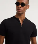 Remera negra de algodón peruano, corte slim, con cuello padre y cierre frontal parcial de cremallera metálica, de manga corta.