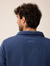 Campera de polar color beige con cierre frontal completo y cuello alto. Presenta un bolsillo en el pecho con cierre y detalle de parche con logo. El diseño combina paneles de tejido polar con detalles en tejido técnico en la zona del pecho.