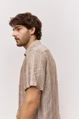 Camisa de manga corta con diseño a rayas verticales en tonos tostado, blanco y azul. Cuenta con cuello clásico y cierre frontal de botones.