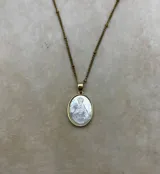 Collar de cadena dorada con eslabones pequeños y detalles de esferas, que sostiene un dije circular con la imagen de la Virgen tallada sobre una base de nácar y borde metálico dorado.