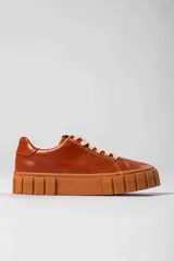 Tenis color marrón con cordones blancos, suela gruesa y texturizada.