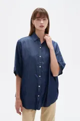 Camisa azul de jean de manga corta, corte holgado, con cuello camisero y cierre frontal con botones.