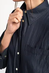 Camisa azul marino de corte oversize, con cuello clásico, cierre frontal con botones, mangas largas con puños anchos y un bolsillo aplicado en el pecho.