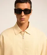 Campera color beige claro de algodón con textura arrugada, cuello inglés, cierre con cremallera, bolsillos laterales, elástico en la cintura y puños.