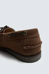 Zapato tipo náutico confeccionado en piel con acabado en serraje. Presenta horma redonda, cordones de cuero y suela con ligero tacón.