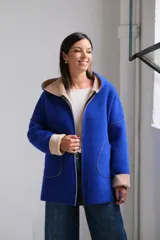 Tapado de paño color azul con capucha, cierre frontal y detalles en color beige en el interior de la capucha, puños y bordes de los bolsillos.